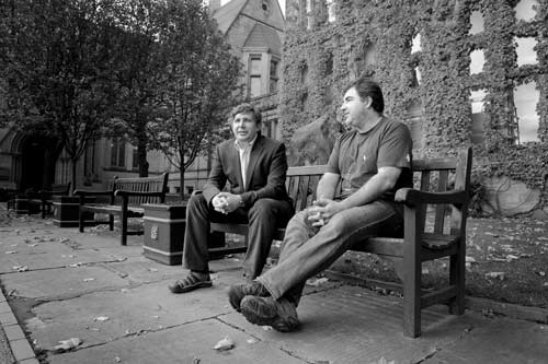 Black and white photo of two men sitting on a bench outside of our university's building.