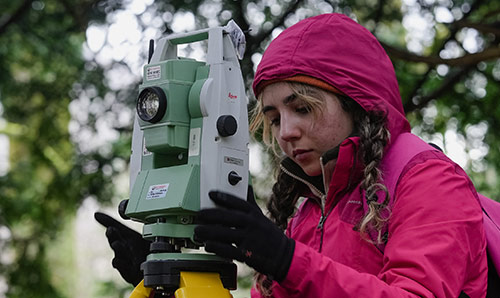 student using surveying equipment on a civil engineering field trip