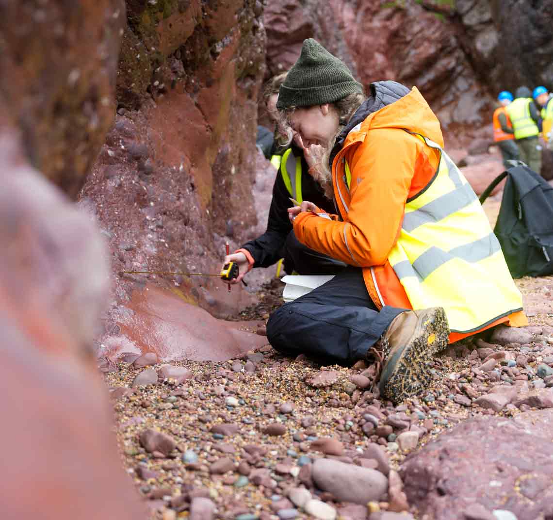 From a class field trip, two researchers holding a tape measure against a rock mountain