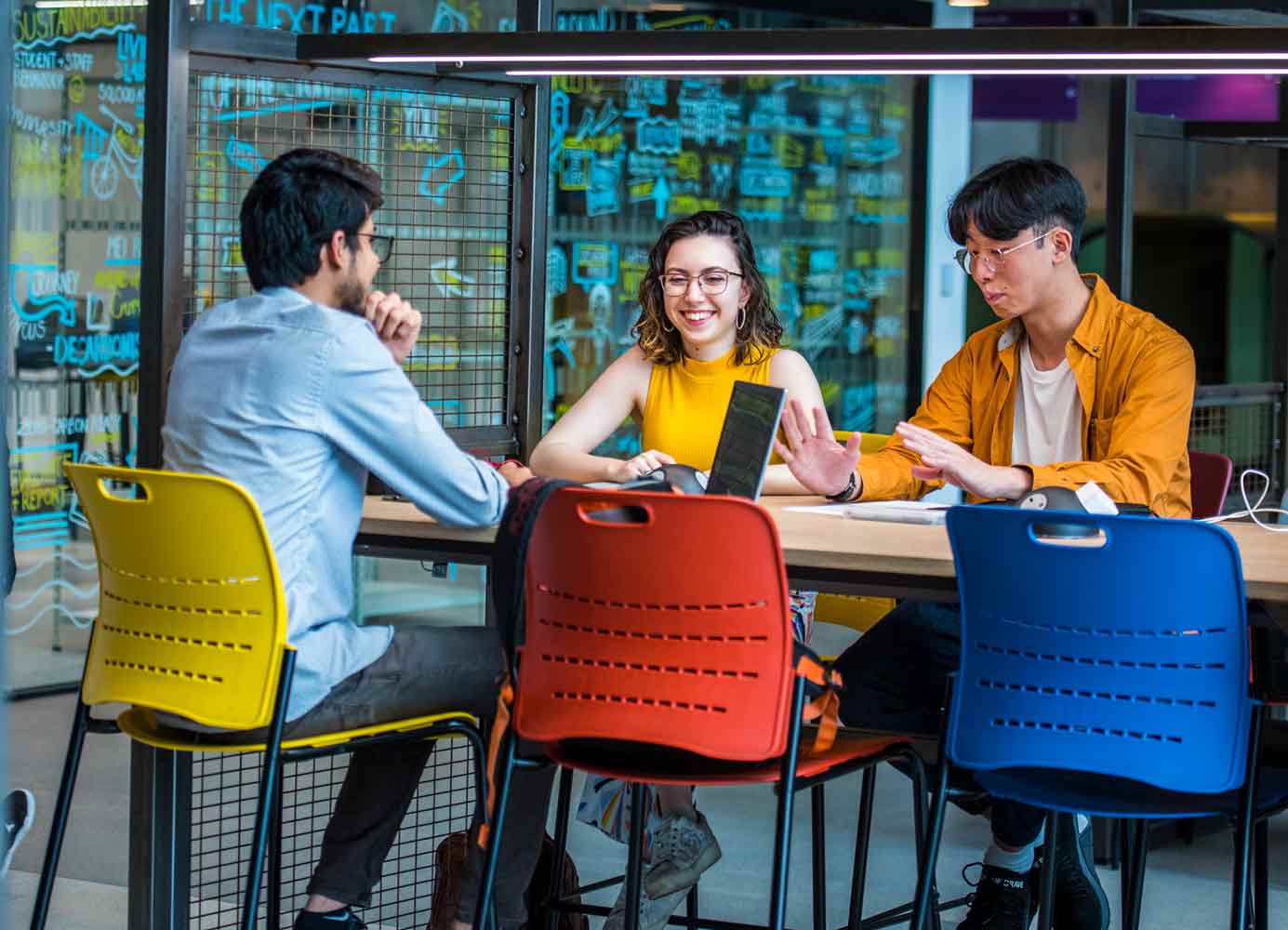 Three students engaging in conversation sat around a table on campus.