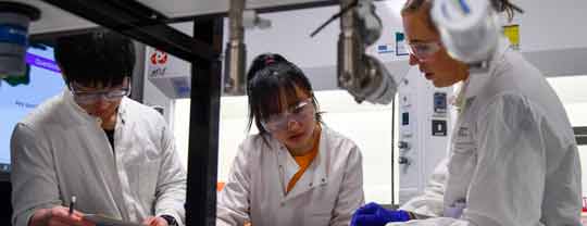 Three students in a lab wearing lab coats