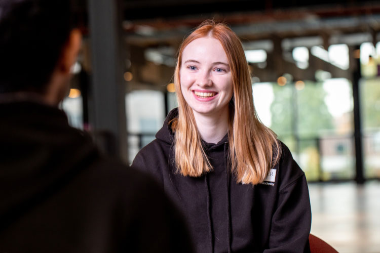 A student at The University of Manchester in a black jumper smiling at another student.