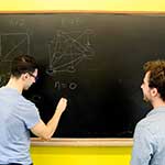 Two students writing an equation on a chalk board